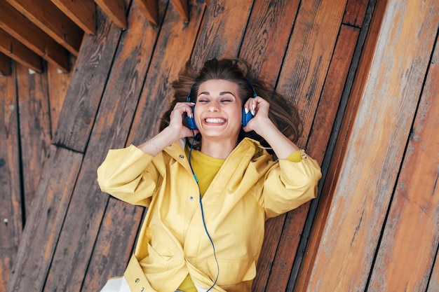 Photo closeup sensual portrait of young smiling happy woman posing with blue earphones outdoor