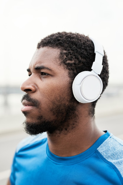 Closeup of serious athlete in wireless headphones listening to music during sports training outdoors