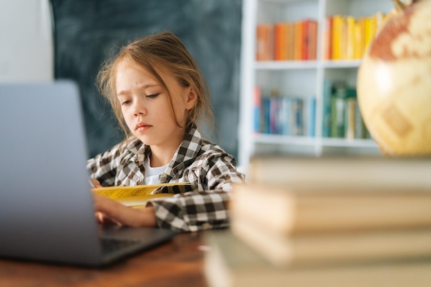 Closeup of serious unhappy elementary child school girl doing writing homework holding pen sitting