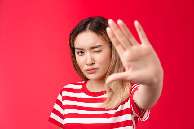 Primo piano serio dall'aspetto determinato donna bionda asiatica tirare la mano in avanti mostra stop tabù segno concentra...