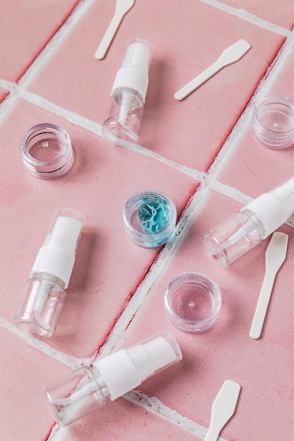 Closeup of set of travel size cosmetic bottles and spatulas Flat lay of cream jars Top view of skin care style concept on pink tile background