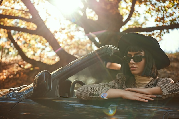 Closeup of sexy lady in sunglasses and hat is sitting in cabriolet