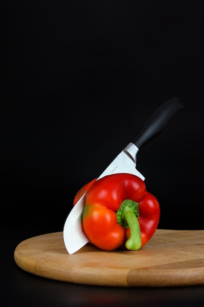 Closeup of Sharp Knife cutting red pepper on wooden board