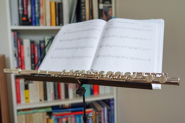 Близкий кадр блестящей флейты на фоне музыкальной партитуры с книжной полкой на заднем плане