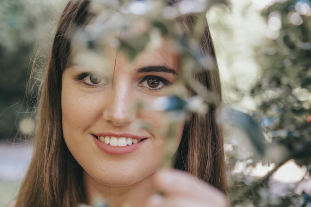 Closeup shot of an attractive brunette girl behind the branches of the tree in the park
