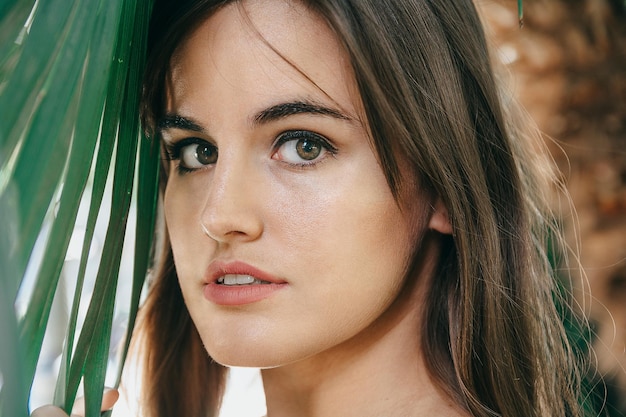 Closeup shot of an attractive brunette girl with a perfect skin near the green plant