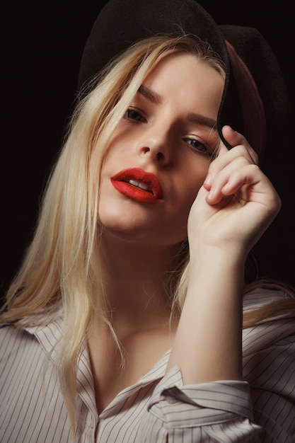 Closeup shot of awesome blonde woman in glasses and hat,  posing with dramatic light at studio