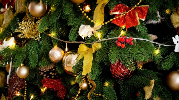 Closeup shot of beautiful decorated Christmas tree with lots of baubles, light garlands and ribbons. Winter holidays background or backdrop.