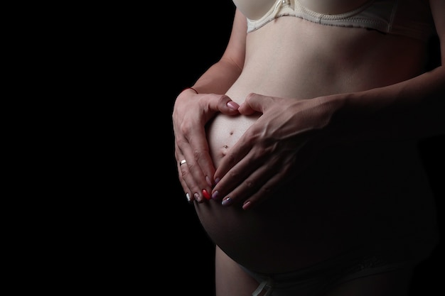 Closeup shot of a belly pregnant girl in white shirt on dark isolated