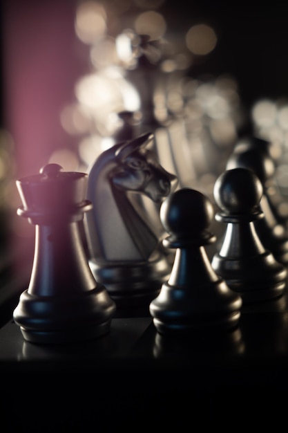 Closeup shot of the black chess pieces on the board with bokeh lights