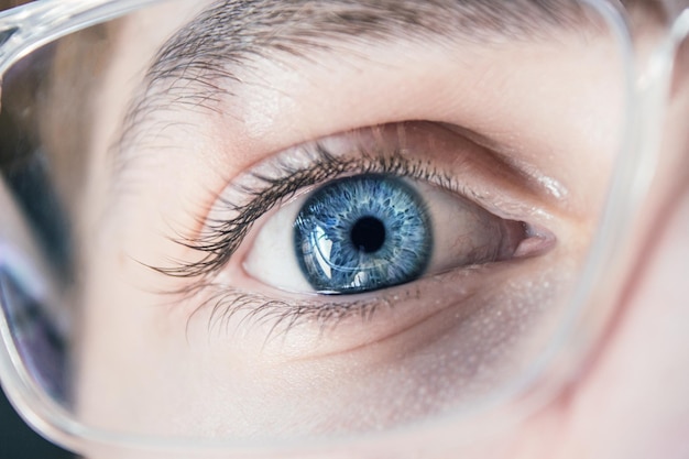 Foto primo piano di un occhio umano blu che indossa occhiali ottici concetto di oftalmologia