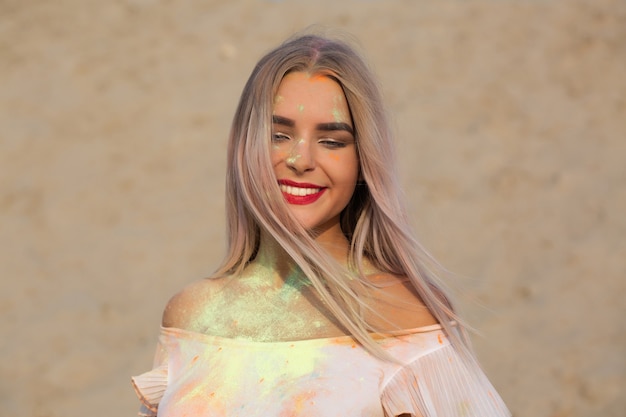 Closeup shot of charming blonde model covered with green dry paint Holi at the desert