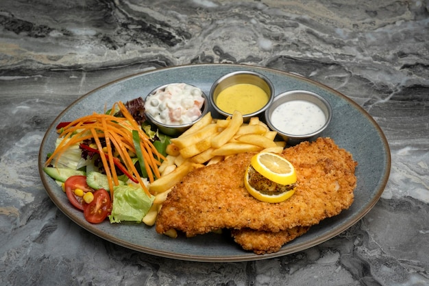 Closeup shot of Chicken schnitzel and fried potatoes on a plate over a marble background