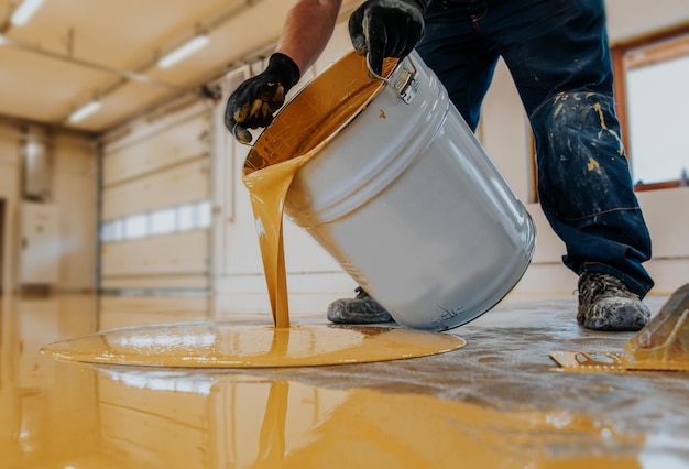 Photo closeup shot of a construction worker pouring out epoxy resin from a bucket onto a floor