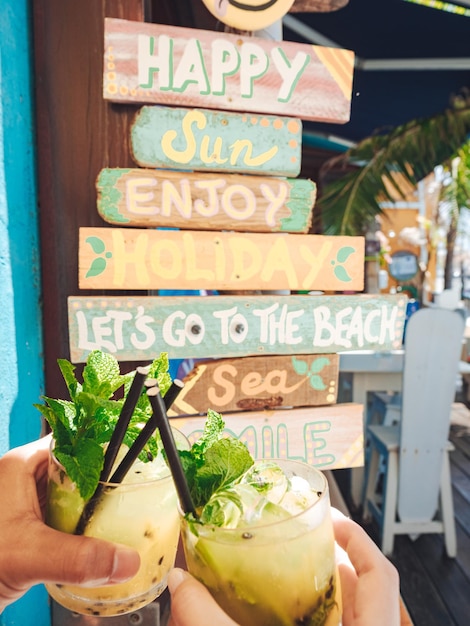 Closeup shot of a couple's hands toasting their cocktails against wooden quote poster background