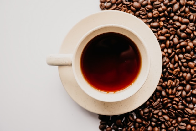 Foto colpo del primo piano di una tazza di caffè con i chicchi di caffè su bianco