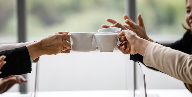 Photo closeup shot of cups of coffee in hands of unrecognizable unidentified businesswoman colleague group in formal business clothing cheering toasting celebrating together after finish planning working.