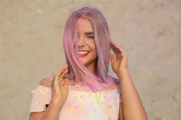 Foto primo piano di una modella bionda espressiva con rossetto rosso ricoperto di vernice secca rosa holi al deserto