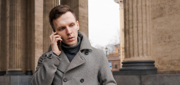 남자의 코트를 입고 그의 휴대 전화를 사용하여 근접 촬영 샷 유행 젊은 남자
