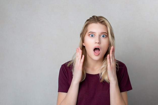 Closeup shot of fearful blonde girl standing over a grey wall. Space for text