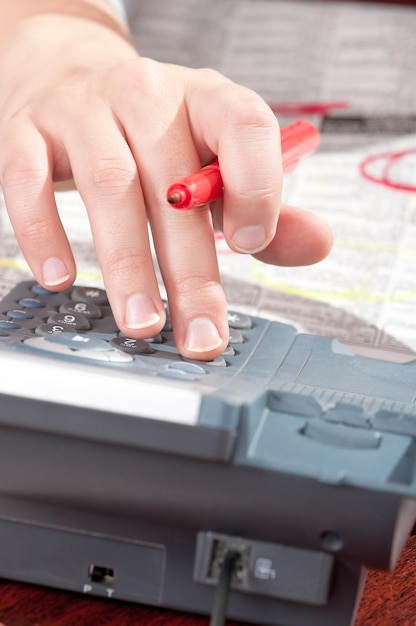 Closeup shot of female finger pressing landline phone numbers Human hand with red marker and telephone Woman searching for ads and job in the newspaper