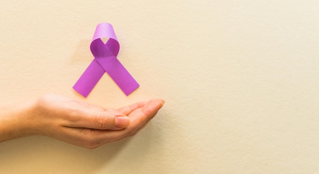 Closeup shot of a female hand holding a purple ribbon on brown background