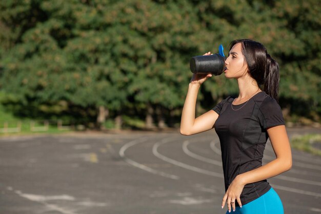 Closeup shot of fitness woman drinking water at the stadium. Space for text