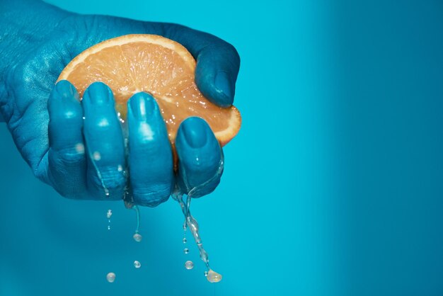 Closeup shot of fresh juice dripping from ripe half of orange while male hand squeezing it against b