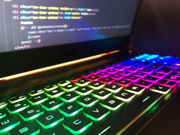 Близкий снимок игровой клавиатуры с RGB-светом на размытом мониторе