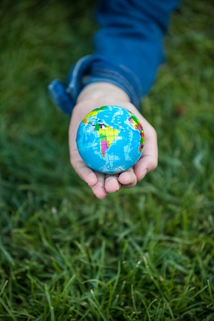 Closeup shot of girl holding small Earth globe in hand against grass background