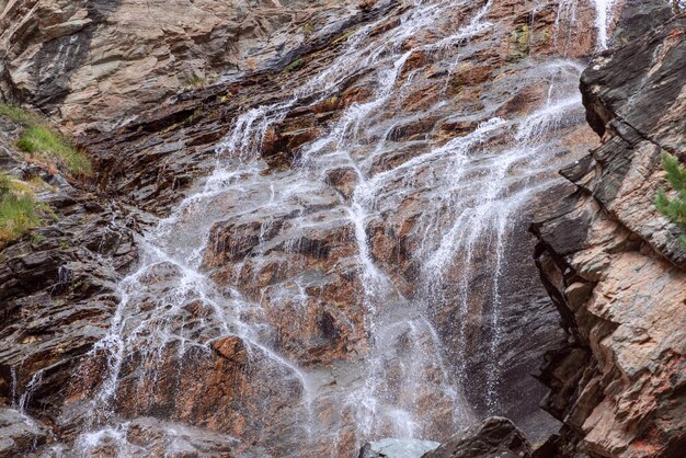 Closeup shot of granite rocks with emerald moss and grass contrasted by alpine waterfall