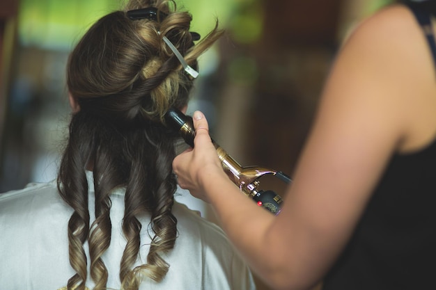 Closeup shot of a hairstylist using a curling wand on a client