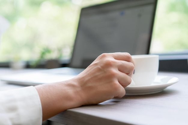 Foto colpo del primo piano della donna della mano che lavora e che tiene il caffè della tazza