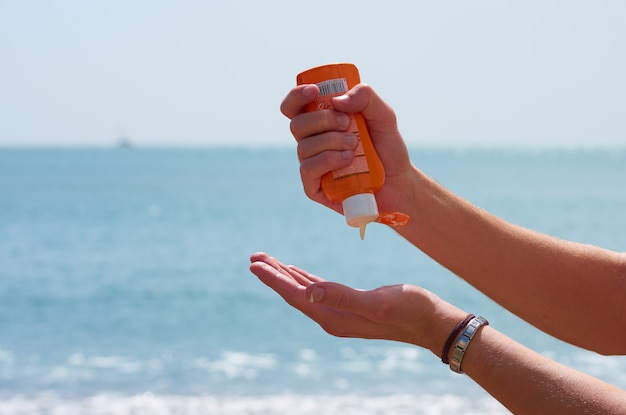 Снимок крупным планом рук, надевающих солнцезащитный крем на пляже