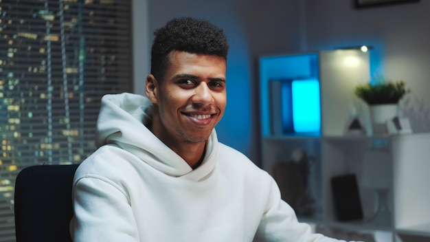 Closeup shot of handsome black man smiling to the camera while working home on computer skyscrapers ...