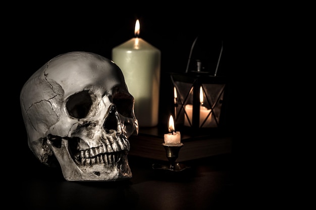 Closeup shot of a human skull and candles on black\
background