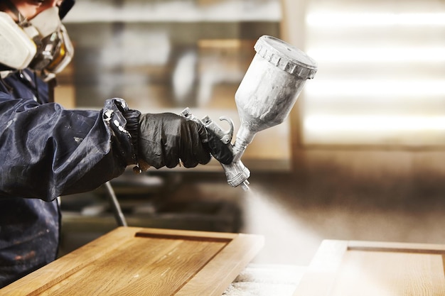 closeup shot of industrial worker using spray gun and painting wood