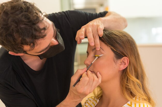 A closeup shot of a male Caucasian makeup artist doing makeup to a Caucasian young female