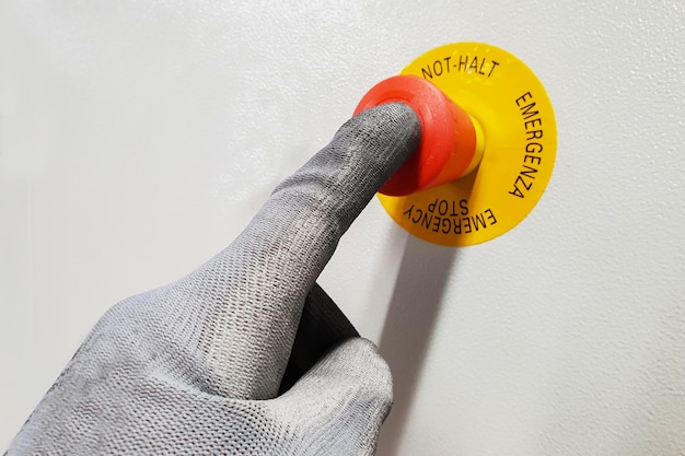 빨간색 응급 정지 버튼에 장갑을 쓴 남성 손의 클로즈업 