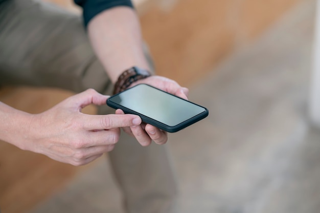 closeup shot of man hands holding blank screen smartphone while sitting outdoors, shallow depth of field.