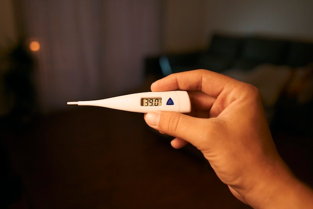 Closeup shot of a man looking at thermometer. Male hands holding a digital thermometer.