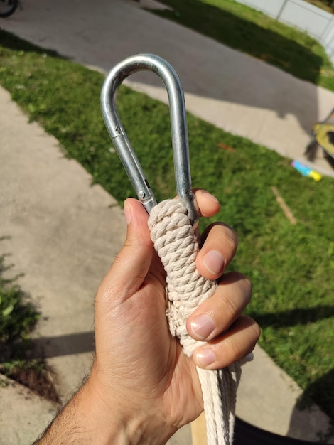 Closeup shot of the man's hand holding a rope with a carabiner hook on the green yard background