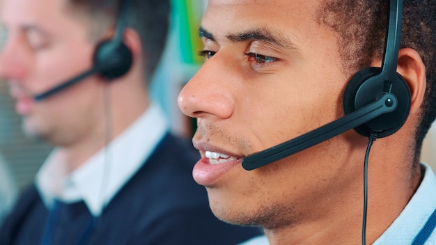 Closeup shot of mixedrace man in headset talking to somebody in office