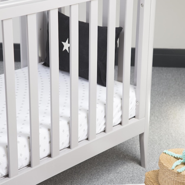 軽い赤ちゃんの部屋で柔らかい枕をかぶった現代的な快適な白塗りのベッドのクローズアップショット