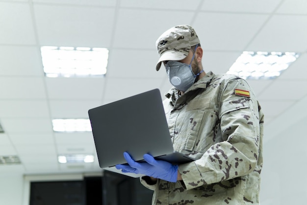 Снимок крупным планом военного мужчины в форме с медицинскими перчатками, использующего свой ноутбук