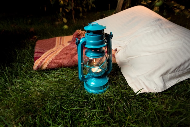 Снимок крупным планом старой масляной лампы, стоящей на траве рядом с подушкой и одеялом