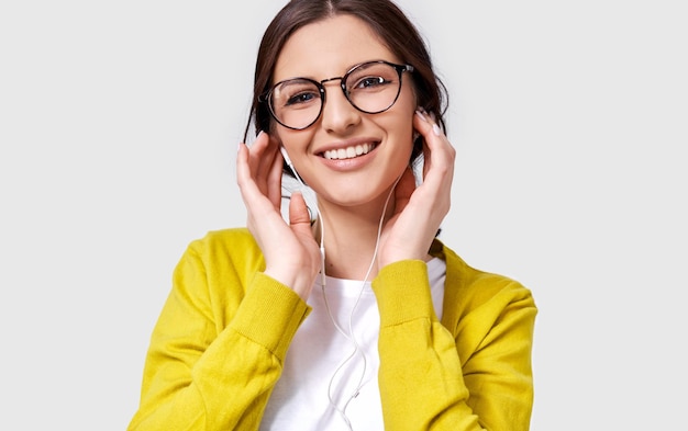 Closeup shot of pretty Caucasian young woman smiling broadly listening the music on headphones Happy female enjoying the favorite songs on earphones People music and technology concept