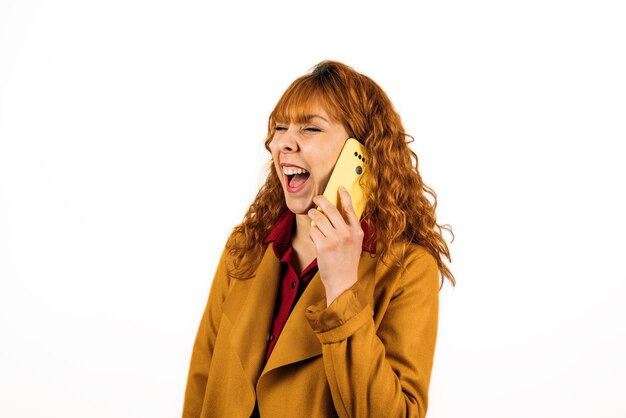 A closeup shot of a redhead woman talking on the phone on an isolated white wall