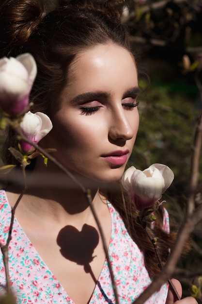 Closeup shot of sensual brunette woman standing near blooming magnolia flowers