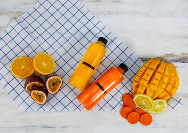 Foto colpo del primo piano della bevanda fredda tropicale estiva bottiglia di succo misto con frutta fresca matura cruda affettata mango arancia limone e frutto della passione posta su un tovagliolo